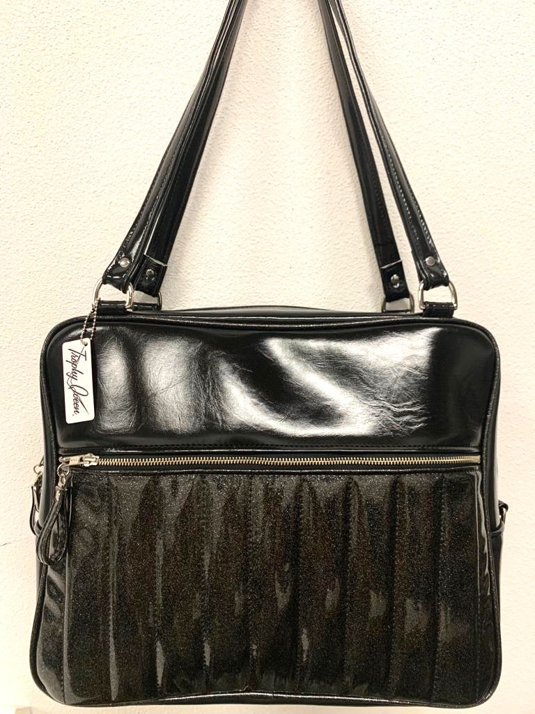 Fairlane Overnight Bag with Coal Black Glitter Vinyl and Grease Black lined with plush Leopard fabric. Handcrafted in California the Fairlane Overnight Bag measures 16”x12”x7” (at the bottom and 5” at the top) with 29” straps and nickel hardware. Detachable Cross Body Strap and extra set of replacement straps included. Inside is two sets of open divided pockets and one zipper pocket with serial number signature Trophy Queen label. Outside your tote is protected with nickel feet and vinyl zipper pull.