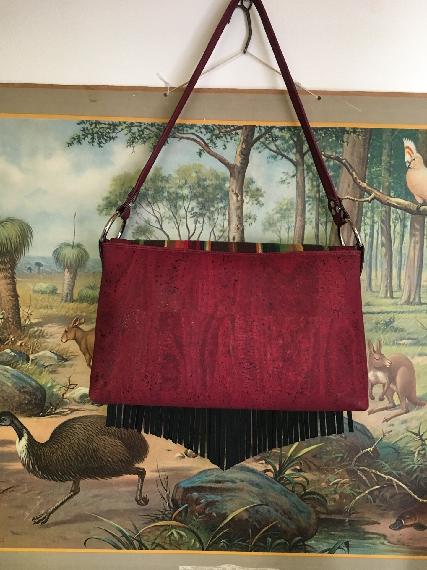 Fringe Saddle Bag in Genuine Sustainable Wine Colored Cork with Chocolate Serape Fabric with 24” (61cm) shoulder strap, magnetic closure, inside open divided pocket and zipper pocket with J.T. Christensen Designs Signature Label and hidden serial number. Ships from Sweden