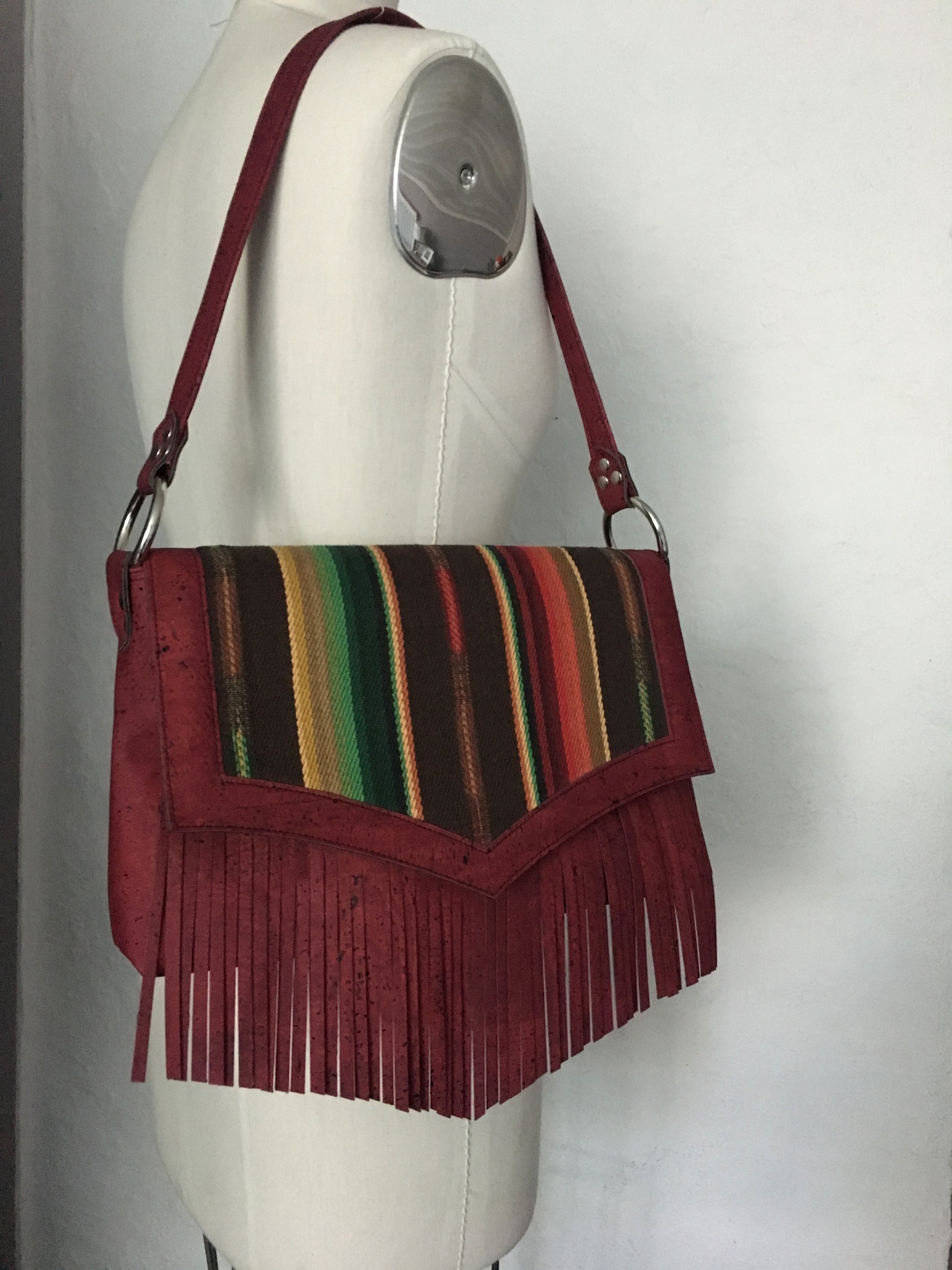 Fringe Saddle Bag in Genuine Sustainable Wine Colored Cork with Chocolate Serape Fabric with 24” (61cm) shoulder strap, magnetic closure, inside open divided pocket and zipper pocket with J.T. Christensen Designs Signature Label and hidden serial number. Ships from Sweden