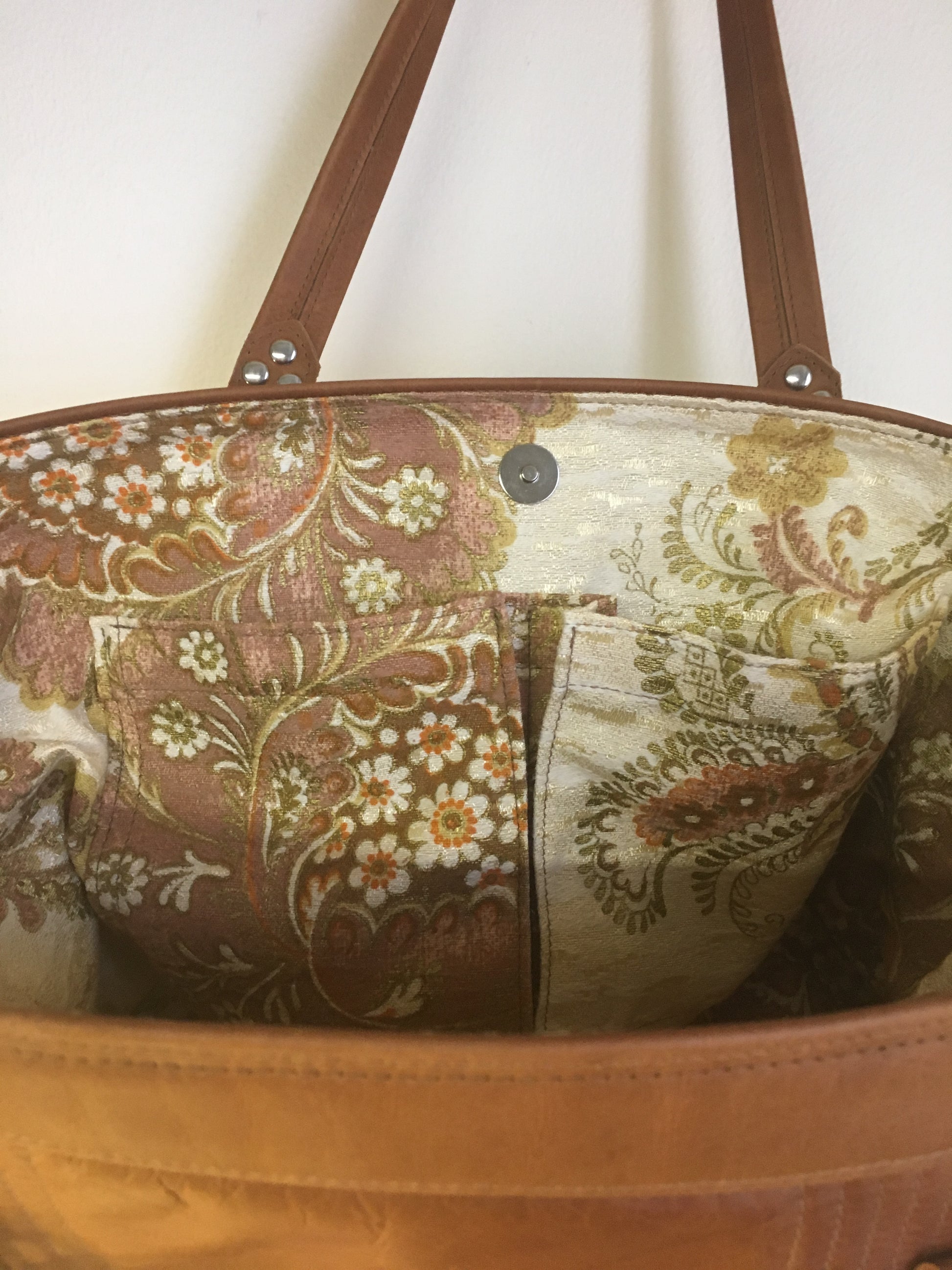 Open Tote with Mercury Style Pleating in Limited Edition Cognac Leather Lined with Re-Purposed 70’s Floral Fabric Lining. Measuring 15” across bottom (19” across top) x 10” x 5” (38 cm At Bottom / 48.25 cm At Top x 25.5 cm Tall x 12.5 cm Wide) and 24” (61cm) Straps. An open divided pocket and zipper pocket with hidden serial number and signature J.T. Christensen Label.
