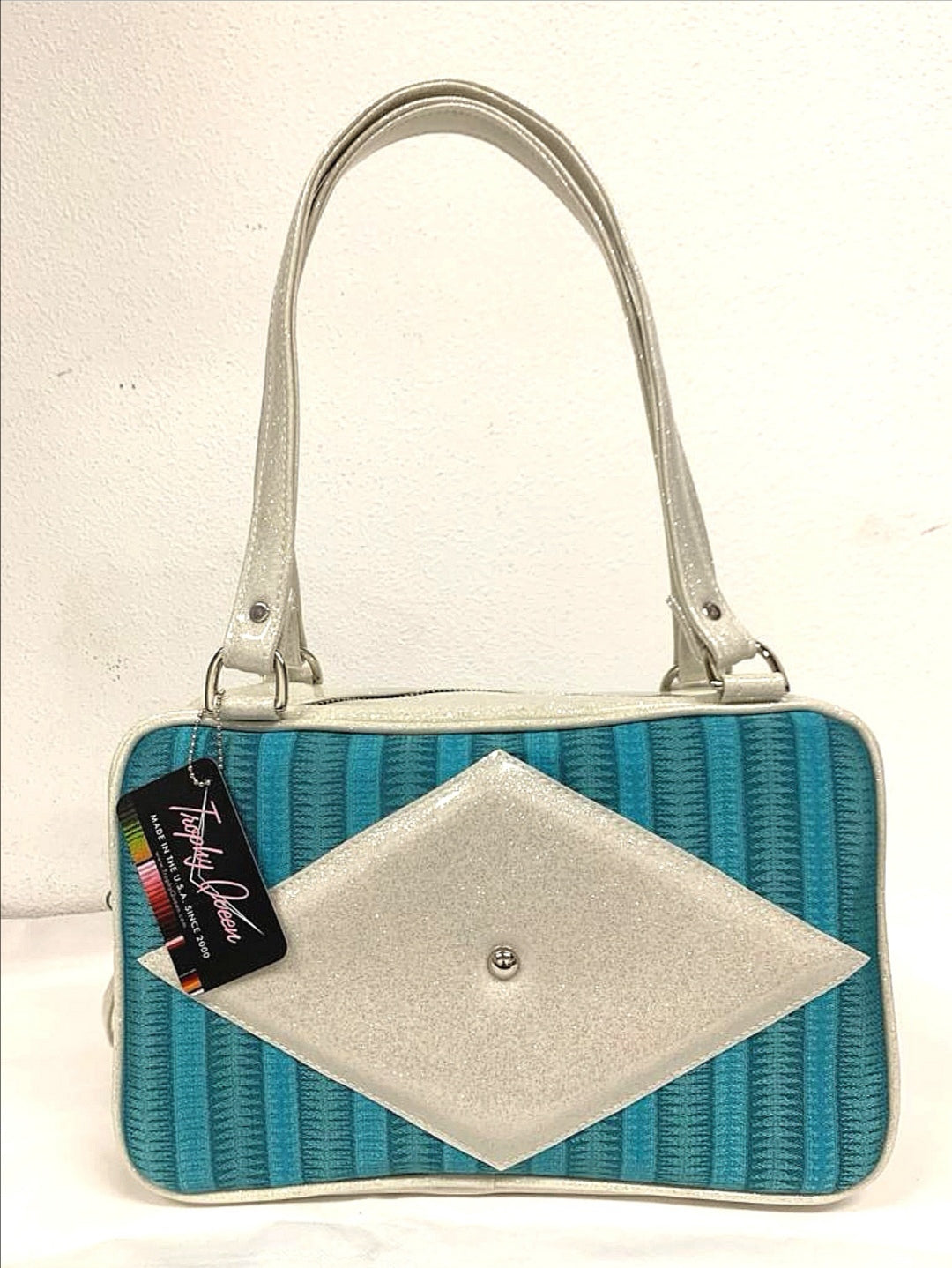 Bel Air Tote with Limited Edition Turquoise '65 Chevy Fabric and White Glitter Vinyl with Plush Leopard Lining. Made from NOS Vintage 1965 Vintage Chevy Upholstery Fabric, this unique bag has matching vinyl zipper pull, nickel feet, inside zipper pocket with serial number and open divided pocket with signature Trophy Queen label. The straps are approximately 25” and come with an extra set of replacement straps. Locally made and ships from California.
