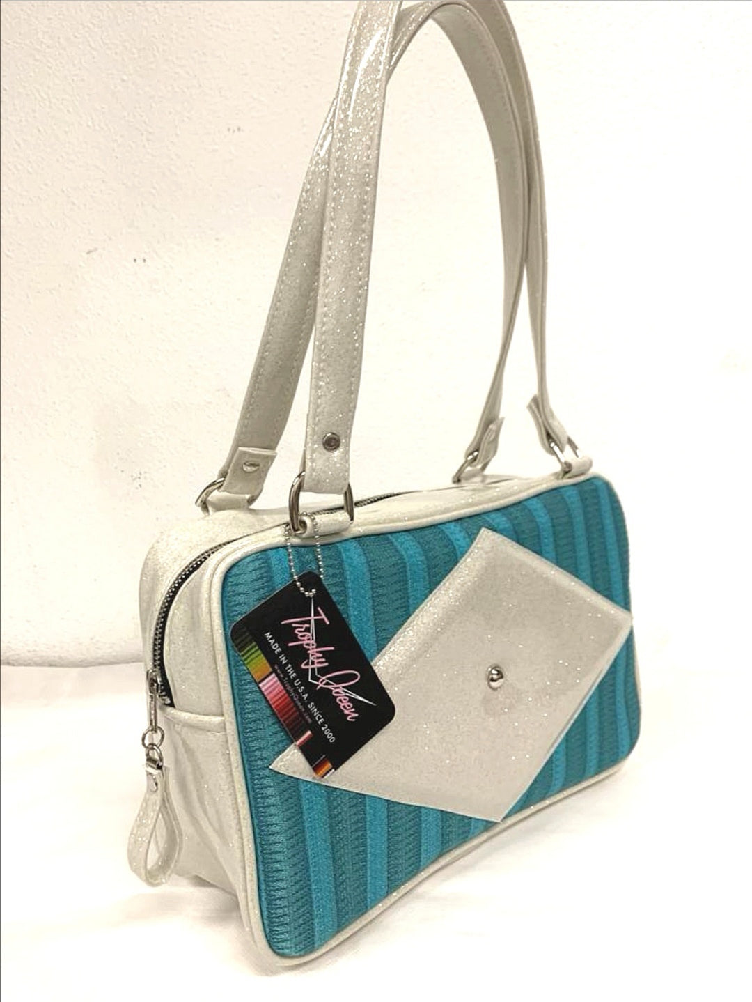 Bel Air Tote with Limited Edition Turquoise '65 Chevy Fabric and White Glitter Vinyl with Plush Leopard Lining. Made from NOS Vintage 1965 Vintage Chevy Upholstery Fabric, this unique bag has matching vinyl zipper pull, nickel feet, inside zipper pocket with serial number and open divided pocket with signature Trophy Queen label. The straps are approximately 25” and come with an extra set of replacement straps. Locally made and ships from California.