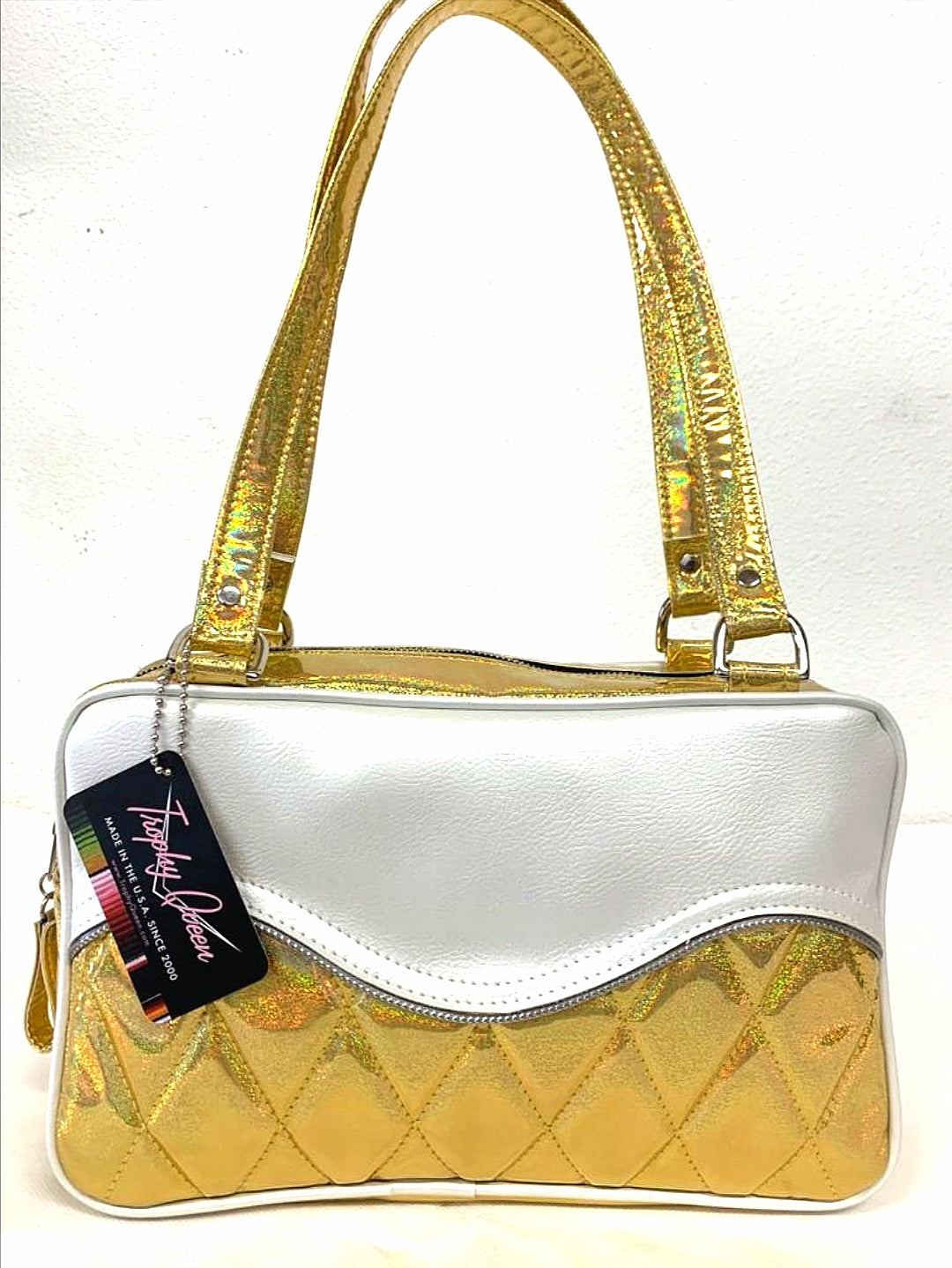 Limited Edition Color the Diamond Pleat Tuck and Roll Tote in Cosmic Gold Glitter and Pearl White Vinyl with plush leopard lining is handcrafted in California with nickel hardware and 25” straps plus it comes with replacement straps. Inside open divided pocket and inside zipper pocket with serial number hidden inside. Nickel feet, vinyl zipper pull, and signature Trophy Queen Label included. The perfect size bag for any trip!