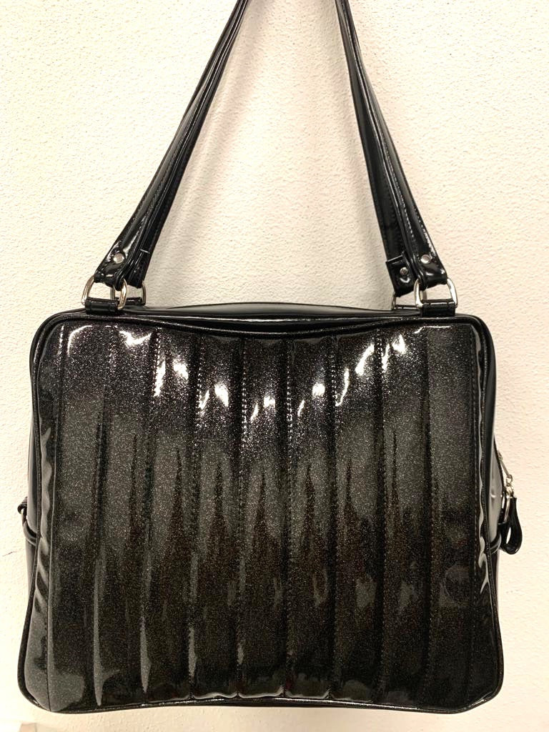 Fairlane Overnight Bag with Coal Black Glitter Vinyl and Grease Black lined with plush Leopard fabric. Handcrafted in California the Fairlane Overnight Bag measures 16”x12”x7” (at the bottom and 5” at the top) with 29” straps and nickel hardware. Detachable Cross Body Strap and extra set of replacement straps included. Inside is two sets of open divided pockets and one zipper pocket with serial number signature Trophy Queen label. Outside your tote is protected with nickel feet and vinyl zipper pull.