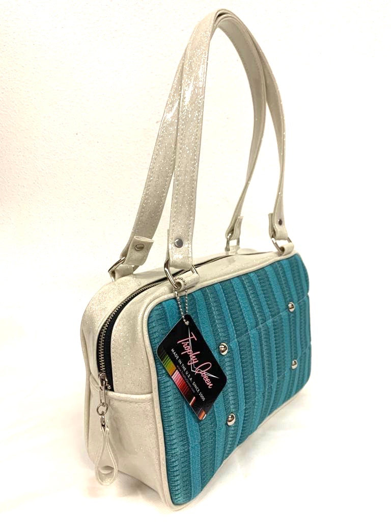 Galaxy Tote, slightly larger than the Galaxy Shoulder Bag in Limited Edition Turquoise ‘65 Chevy Fabric with White Glitter Vinyl and Plush Leopard Lining. Made from NOS Vintage 1965 Chevy Upholstery Fabric with nickel hardware and nickel feet, vinyl zipper pull, and 25” (61cm) straps. Inside you’ll find an open divided pocket, a zipper pocket with serial number inside and signature Trophy Queen Label. Ships from California with an extra set of replacement straps.