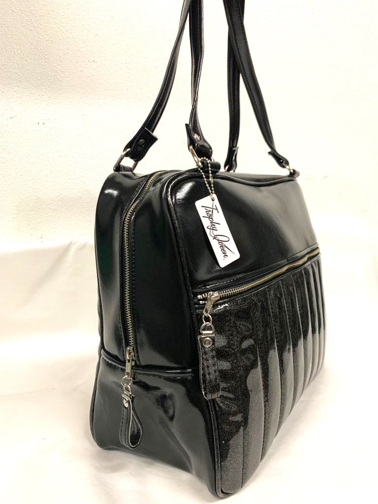 Fairlane Overnight Bag with Coal Black Glitter Vinyl and Grease Black lined with plush Leopard fabric. Handcrafted in California the Fairlane Overnight Bag measures 16”x12”x7” (at the bottom and 5” at the top) with 29” straps and nickel hardware. Detachable Cross Body Strap and extra set of replacement straps included. Inside is two sets of open divided pockets and one zipper pocket with serial number signature Trophy Queen label. Outside your tote is protected with nickel feet and vinyl zipper pull.