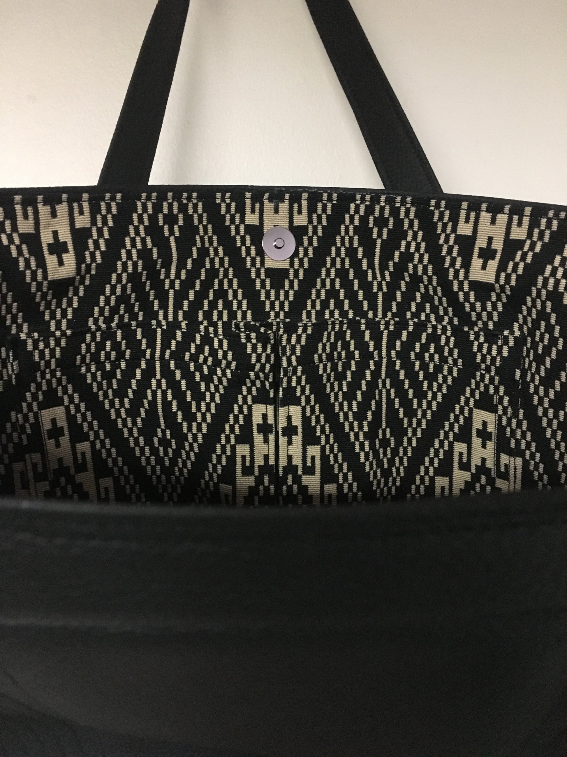 Open Tote with Mercury Style Pleating in Limited Edition Pebble Black Vinyl Lined with Aztec Print Lining. Measuring 15” across bottom (19” across top) x 10” x 5” (38 cm At Bottom / 48.25 cm At Top x 25.5 cm Tall x 12.5 cm Wide) and 24” (61cm) Straps. An open divided pocket and zipper pocket with hidden serial number and signature J.T. Christensen Label.