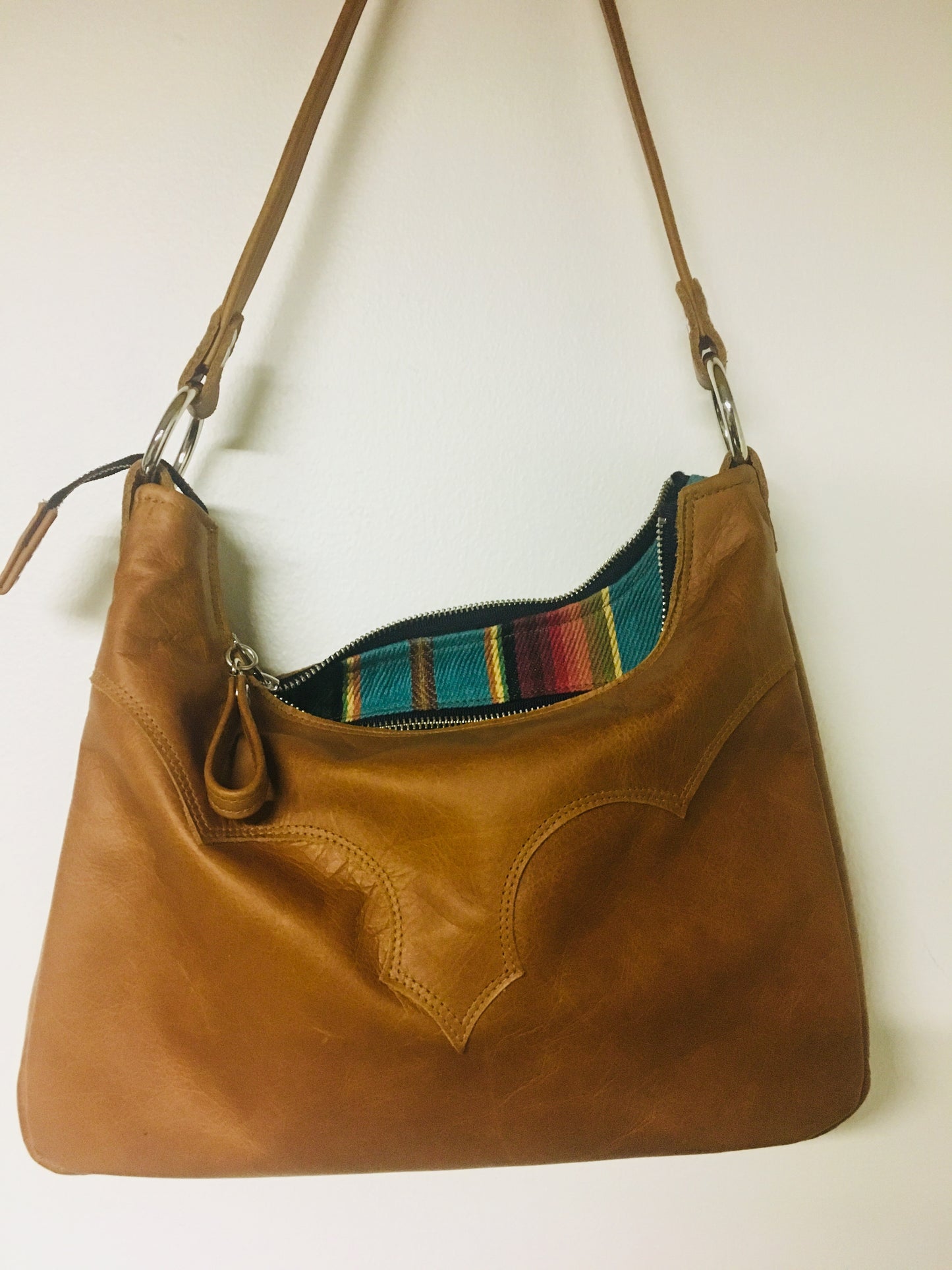Death Valley hobo shoulder bag in Cognac leather and turquoise serapae print lining with zipper closure and vinyl pull, inside open divided pocket and one zipper pocket with 22” shoulder strap. Signature J.T.Christensen Designs Label inside.