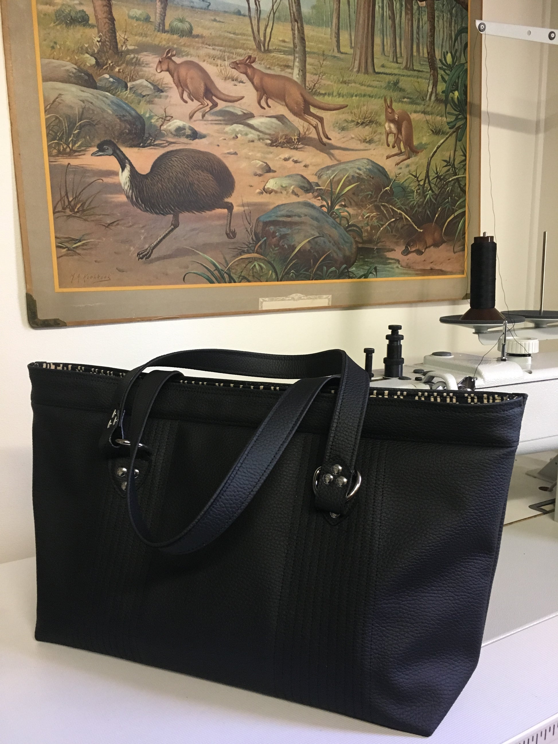 Open Tote with Mercury Style Pleating in Limited Edition Pebble Black Vinyl Lined with Aztec Print Lining. Measuring 15” across bottom (19” across top) x 10” x 5” (38 cm At Bottom / 48.25 cm At Top x 25.5 cm Tall x 12.5 cm Wide) and 24” (61cm) Straps. An open divided pocket and zipper pocket with hidden serial number and signature J.T. Christensen Label.