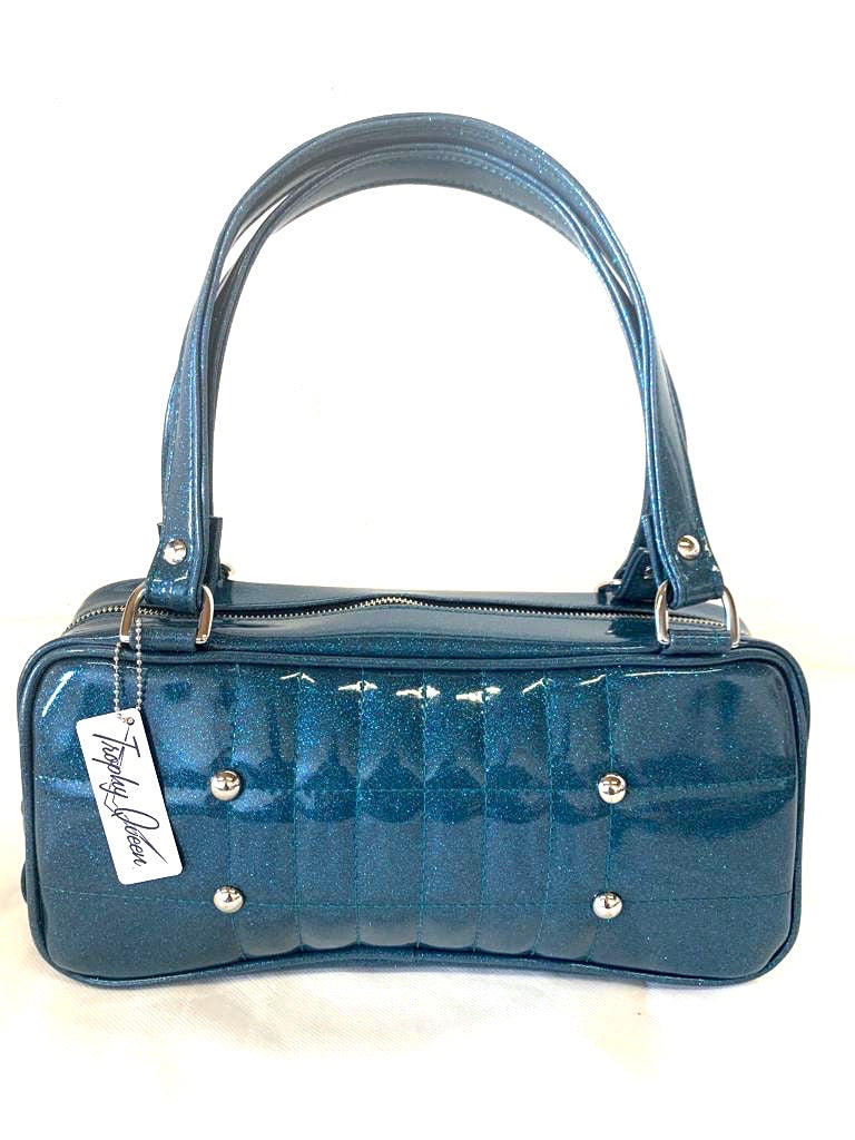 Galaxy Shoulder Bag in Teal Glitter Vinyl and Plush Leopard Lining with nickel hardware and nickel feet, vinyl zipper pull, and 21” (approx 53cm) straps. Inside you’ll find an open divided pocket, a zipper pocket with serial number inside and signature Trophy Queen Label. Ships from California with extra set of replacement straps.