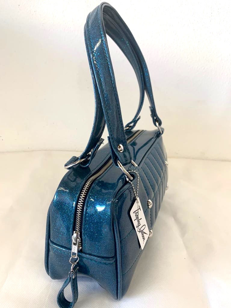 Galaxy Shoulder Bag in Teal Glitter Vinyl and Plush Leopard Lining with nickel hardware and nickel feet, vinyl zipper pull, and 21” (approx 53cm) straps. Inside you’ll find an open divided pocket, a zipper pocket with serial number inside and signature Trophy Queen Label. Ships from California with extra set of replacement straps.