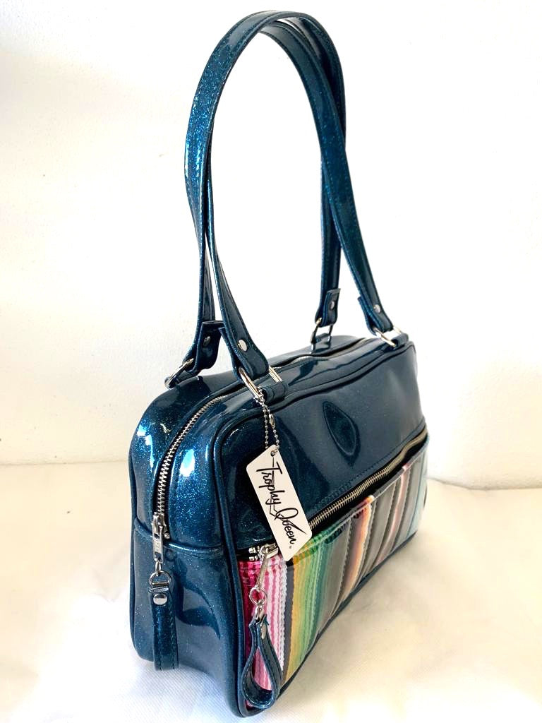 Fairlane Tote Bag in Genuine Mexican Blanket with Clear Overlay and Teal Glitter Vinyl with plush Leopard Lining. This purse has matching vinyl zipper pull, nickel feet, inside zipper pocket with serial number and open divided pocket with signature Trophy Queen label. The straps are approximately 25” and come with an extra set of replacement straps. Locally made and ships from California.